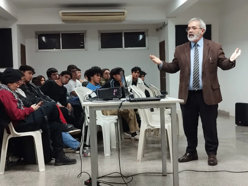 Un docente da clase de pie frente a un grupo de estudiantes con computadoras