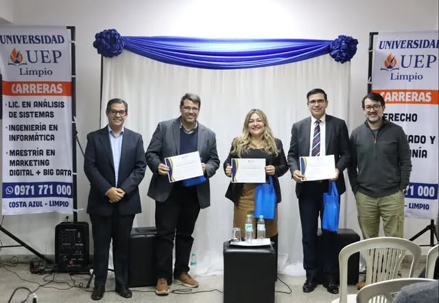 Cinco personas sostienen certificados frente a los banners de carreras del campus