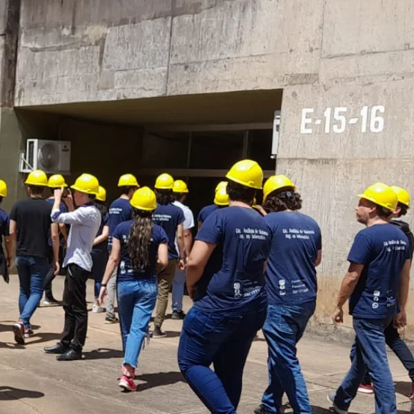 Estudiantes con cascos amarillos y remeras de la FACUTEC entrando a una planta industrial
